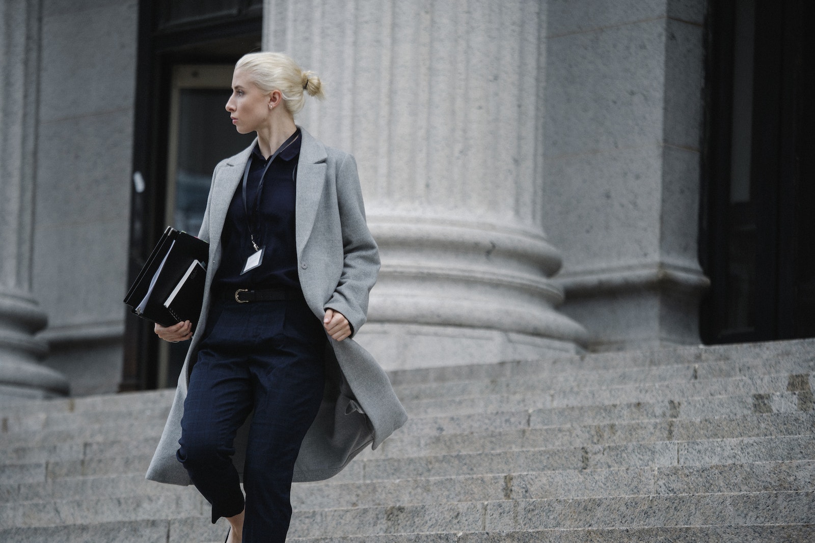 Serious female lawyer in elegant outfit holding folders with documents while going downstairs near stone state building and looking away